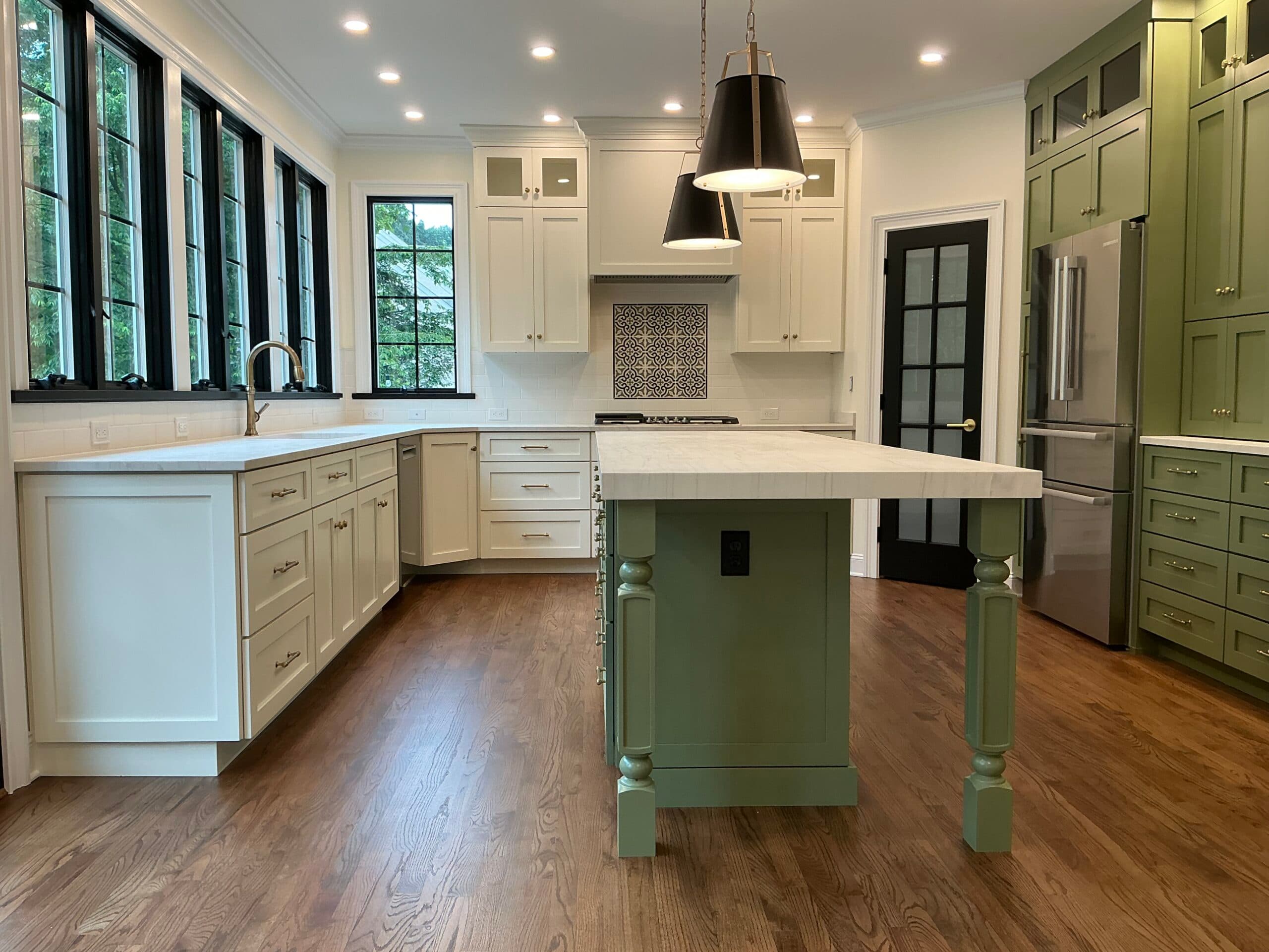 Two-tone designer kitchen with sage green island, black-frame windows, and brass fixtures by Harlan Custom Contracting