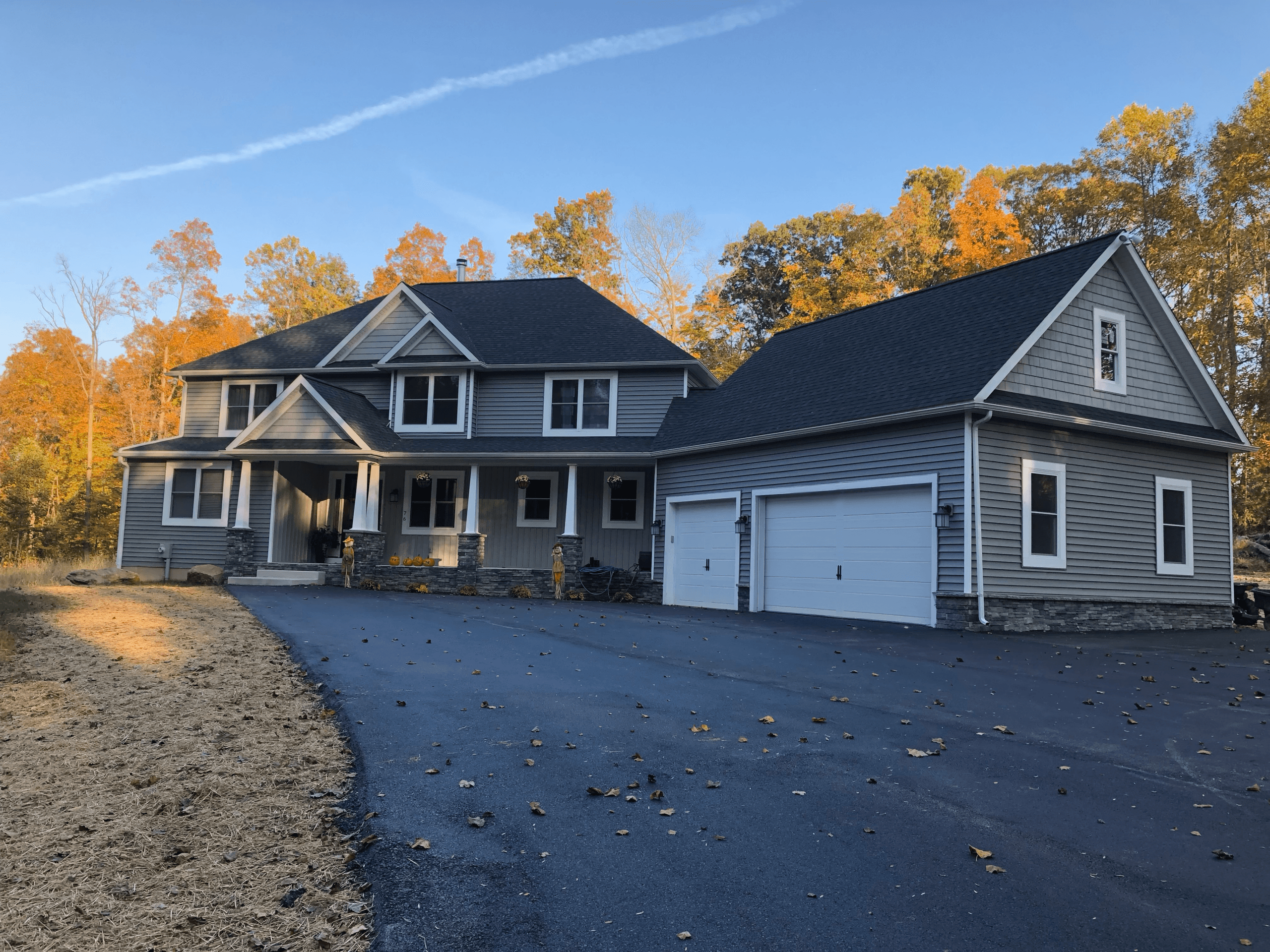 Craftsman-style home exterior with gray siding, stone accents, and black roof by Harlan Custom Contracting