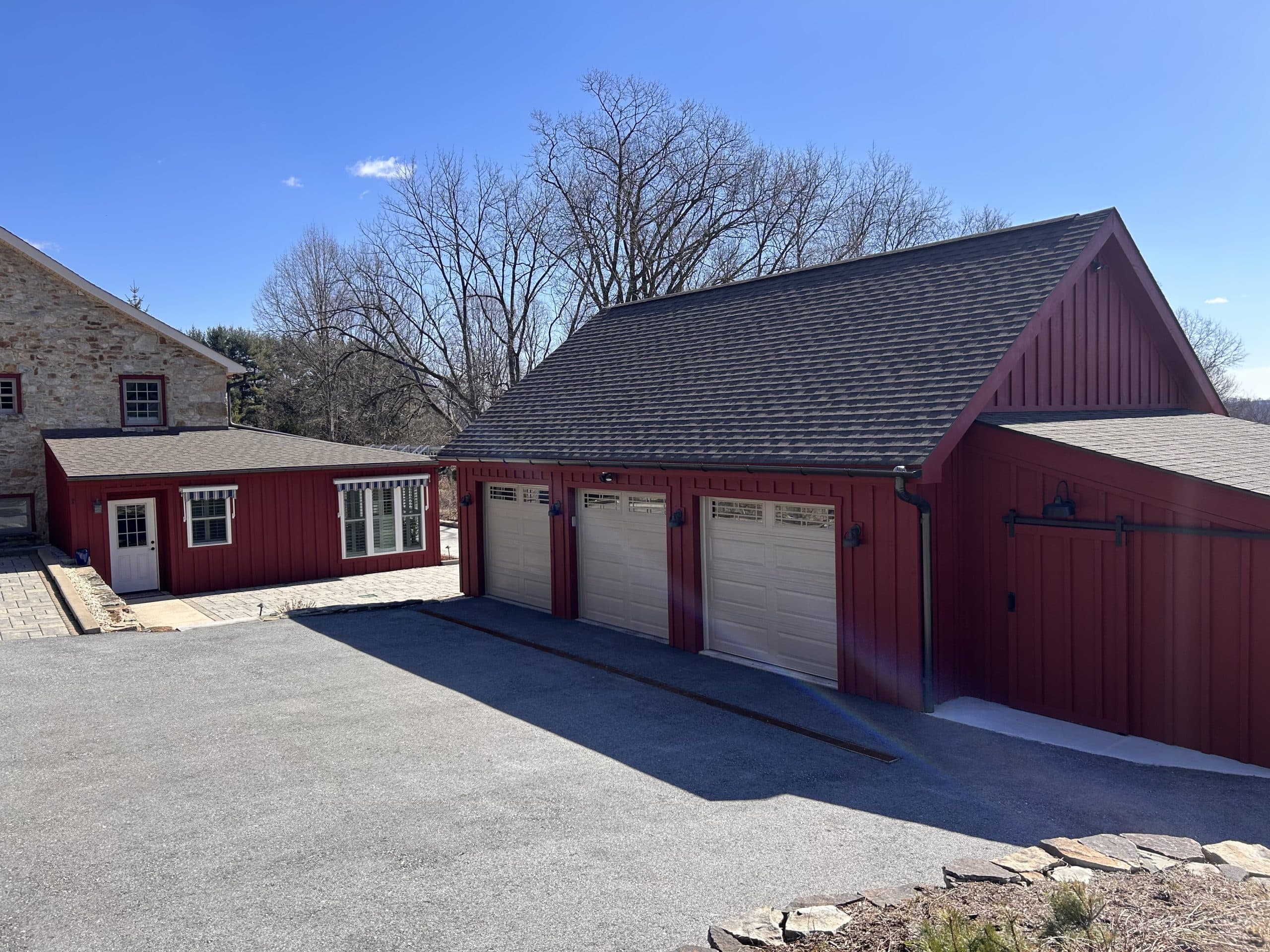 Barn-style three-car garage addition with board-and-batten siding on a stone farmhouse — Harlan Custom Contracting project