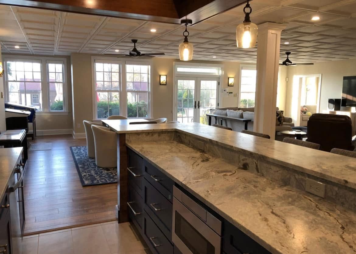 Basement bar with granite counters and under-counter microwave, opening to a sunlit lounge — Harlan Custom Contracting project