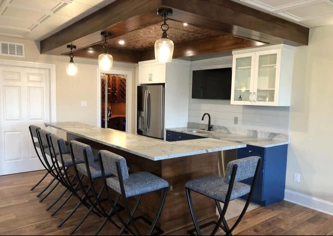 L-shaped basement bar with navy cabinetry, wood ceiling detail, and wine room beyond — Harlan Custom Contracting project