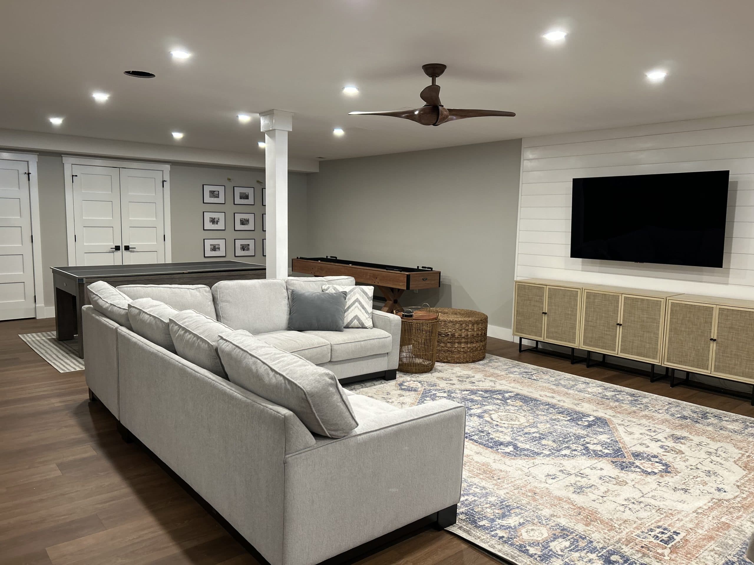 Basement family room with shiplap accent wall, shuffleboard, and game tables — Harlan Custom Contracting project