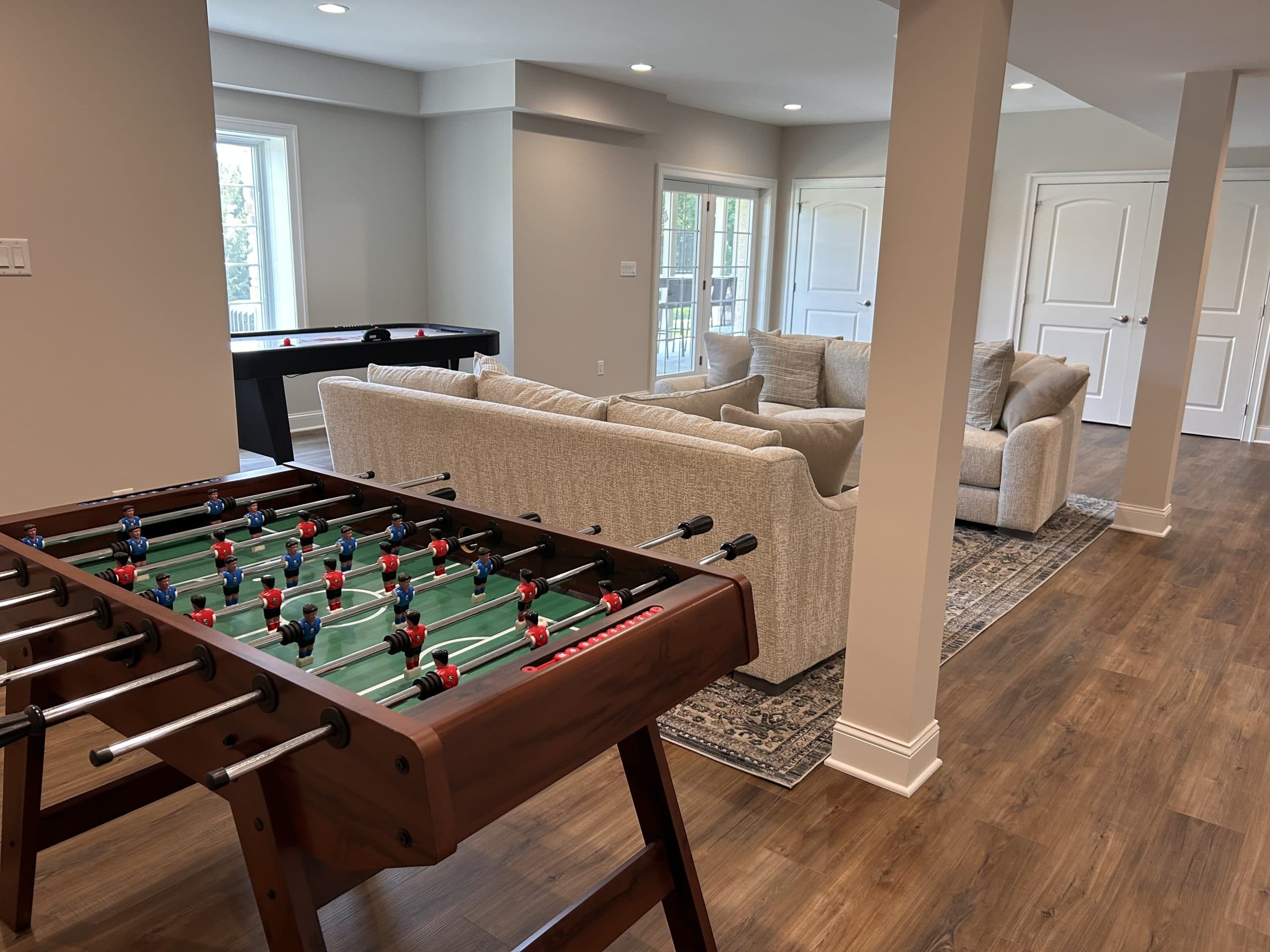 Open basement game room with foosball, air hockey, and lounge seating — Harlan Custom Contracting project