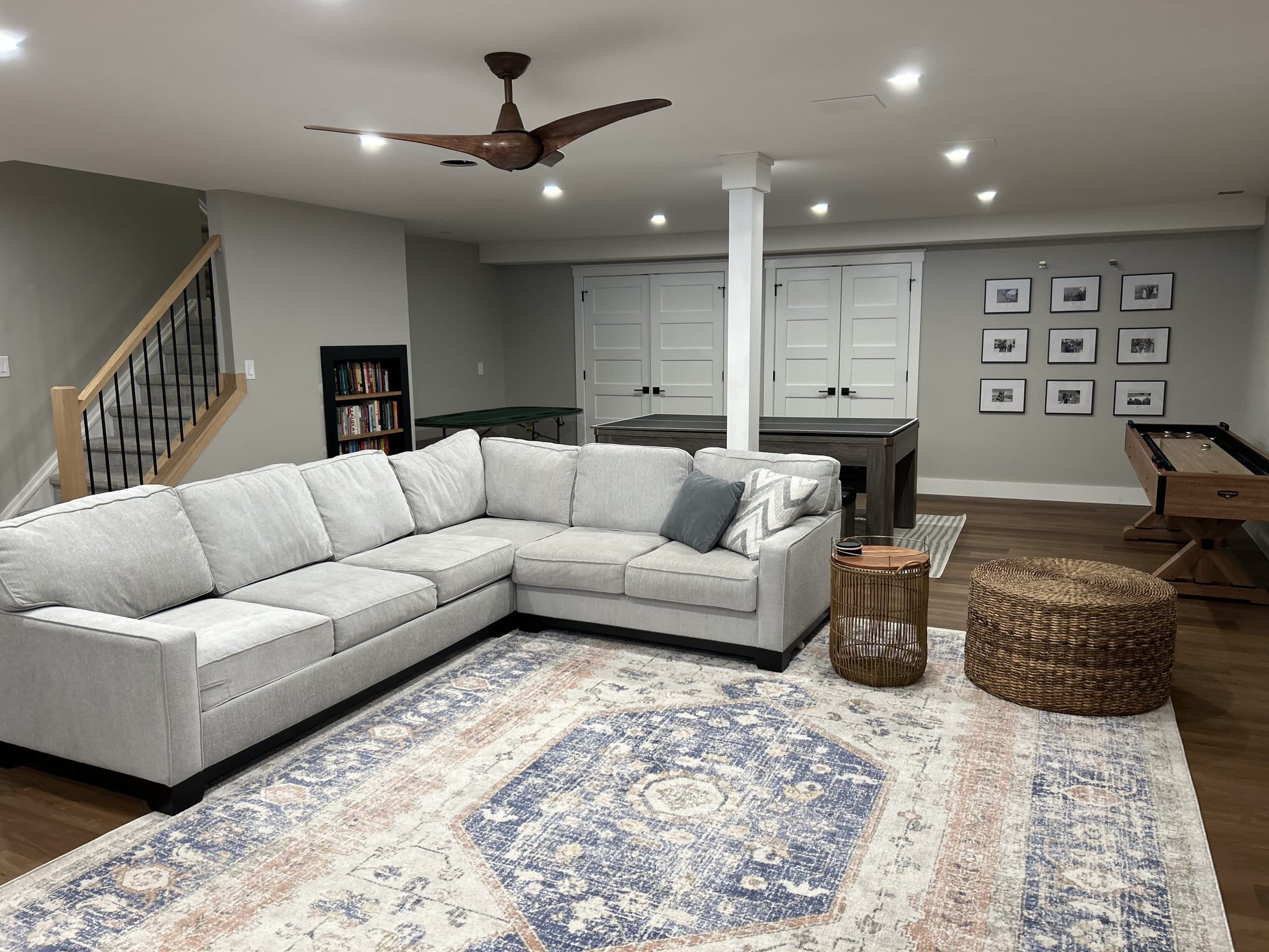 Basement family room with oak staircase, shuffleboard, and gallery wall — Harlan Custom Contracting project