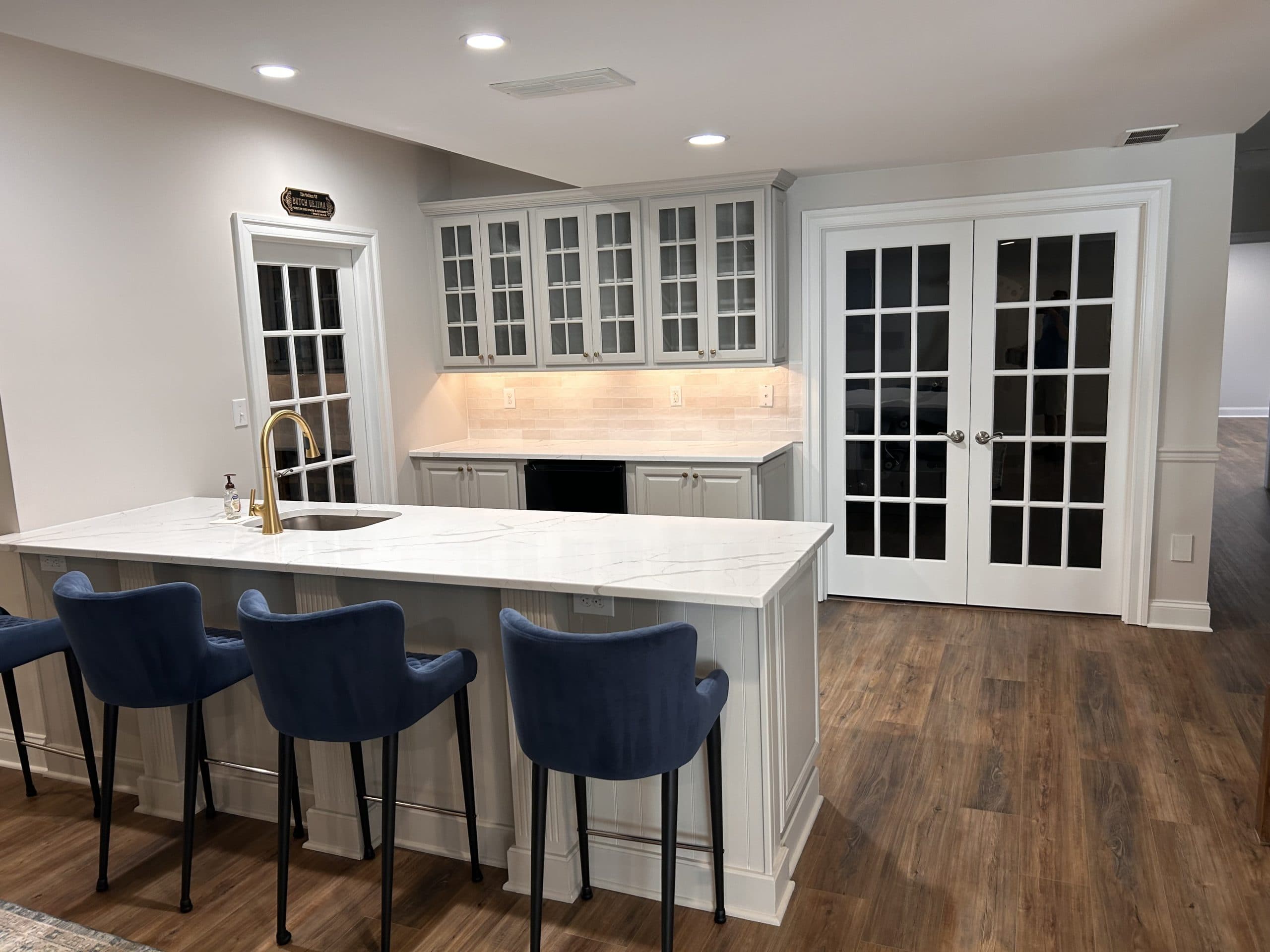 Basement wet bar with glass-front cabinetry, quartz peninsula, and French doors — Harlan Custom Contracting project